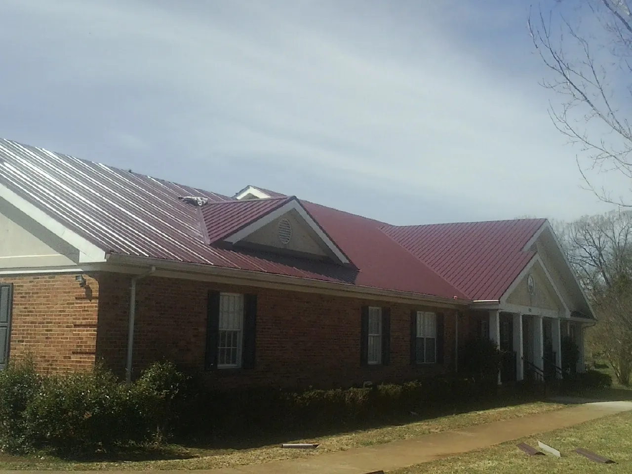 Red metal roof with gabled entries on a long brick building, from a Hail Damage Roof Repair job in Oyens