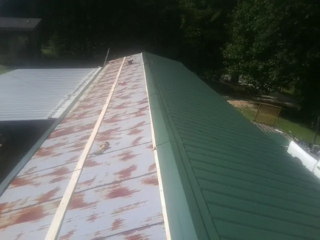 Old rusted panels beside newly installed green metal roofing — Wind Damage Roof Repair by Roofing Brothers in Oyens