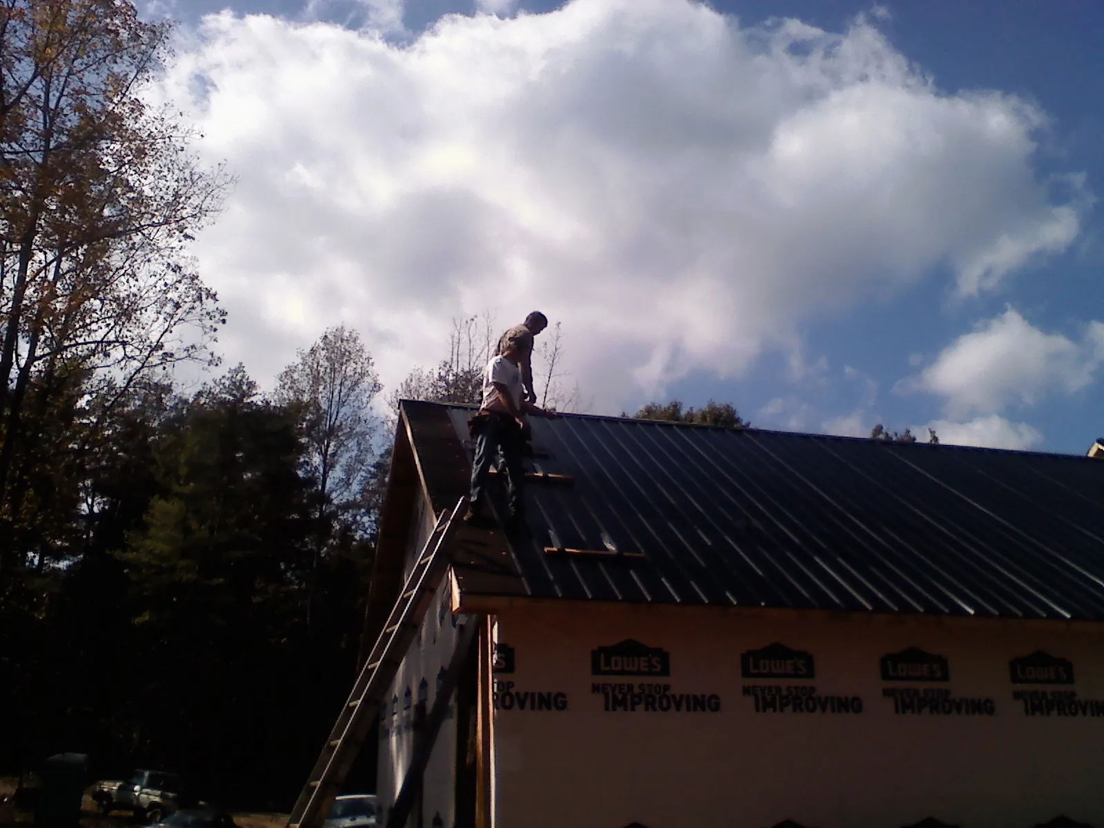 Roofer fastening dark metal panels high against a cloudy sky, from a Roof Inspection job in Oyens
