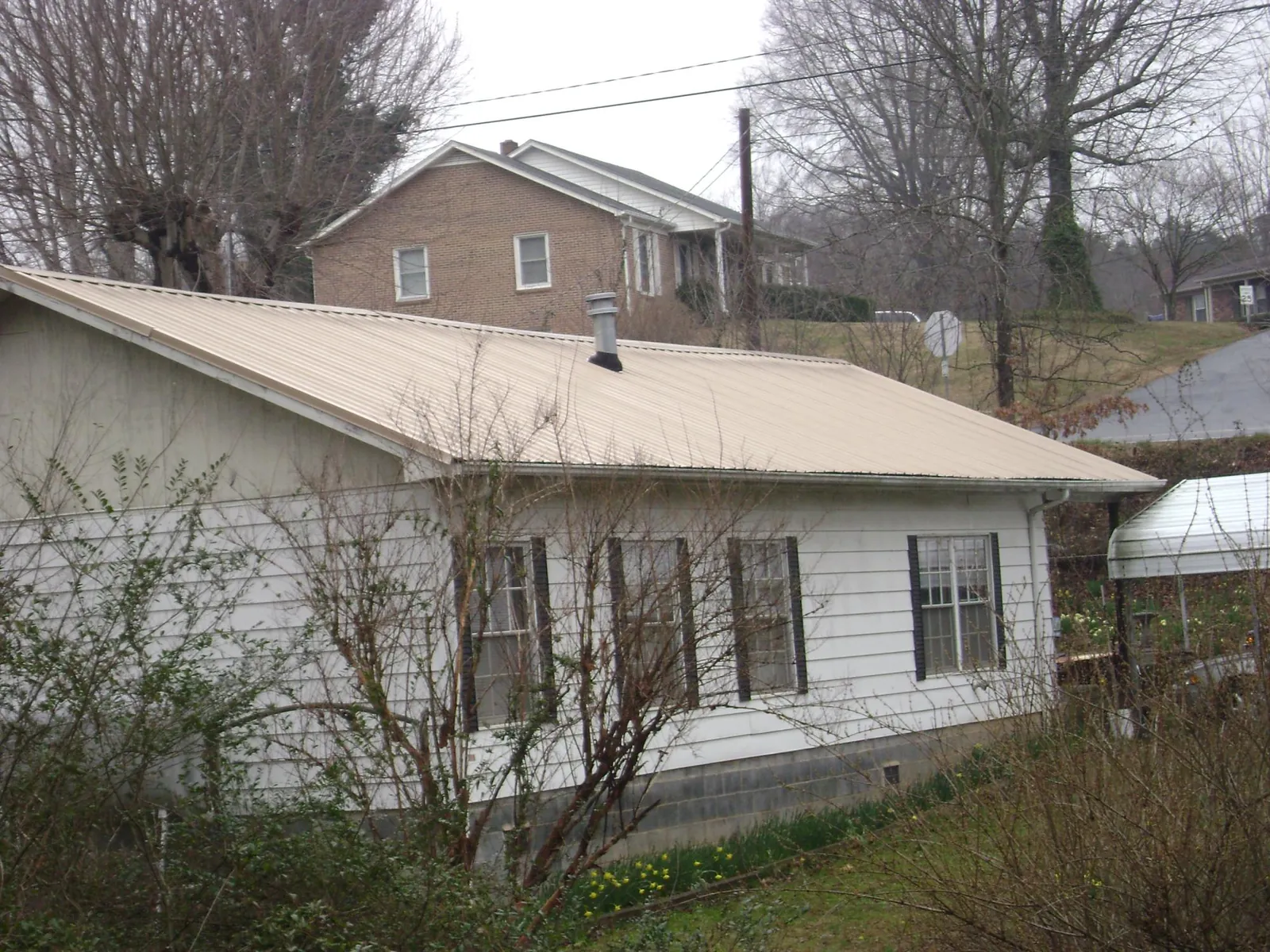 Tan metal roof on a white sided house set into a hillside — Commercial Roofing by Roofing Brothers in Oyens