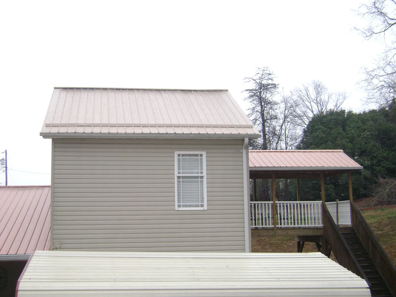 Tan metal roofs on a two story addition and attached porch, from a Roof Replacement job in Oyens